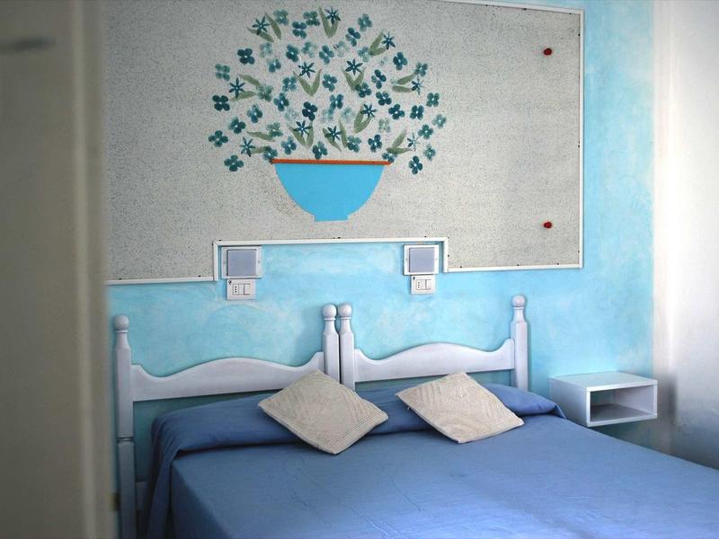 Zweibettzimmer mit blauer Wand, zwei Betten, blauer Bettdecke und Wanddeko mit Blumentopfmotiv.