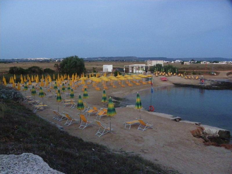 Strand mit Sand, leeren gelb-grünen Sonnenschirmen und Liegestühlen am ruhigen Wasser bei Abenddämmerung.