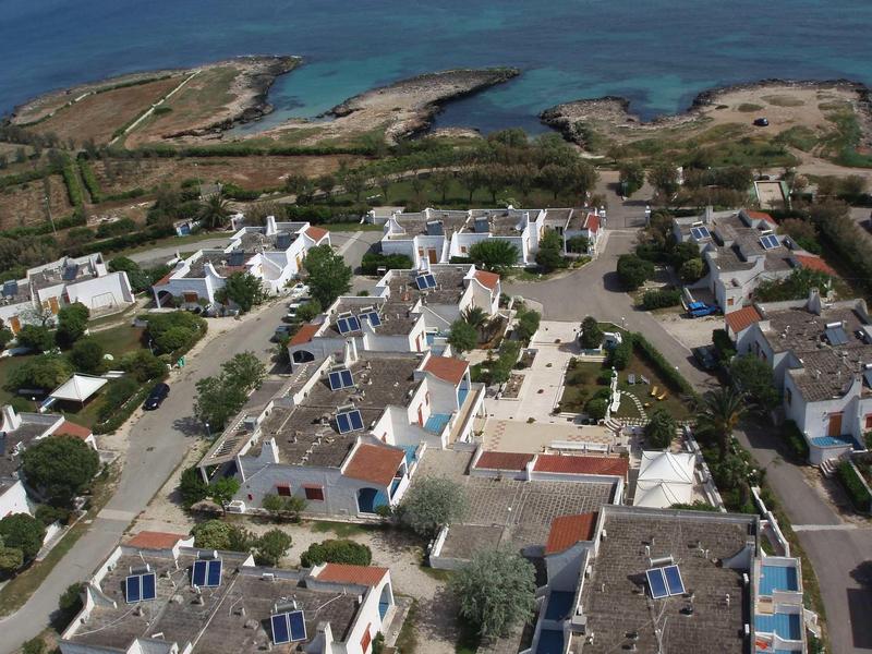 Kleines Dorf mit weißen Häusern, roten Dächern, Bäumen und Küstenlinie im Hintergrund.