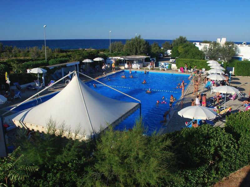 Freizeitbad mit blauem Pool, weißen Sonnenschirmen und Blick auf das Meer im Hintergrund.