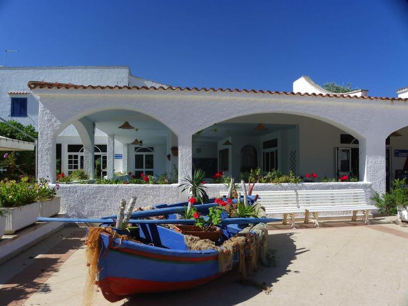 Weißes Gebäude mit Rundbögen und blauen Booten davor unter klarem blauem Himmel.