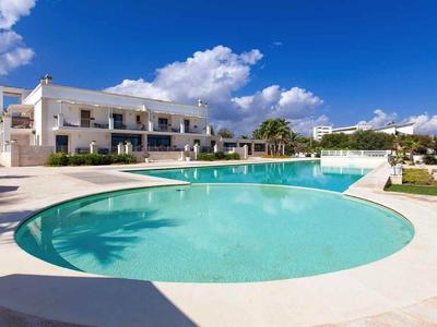 Moderner Wohnkomplex mit rundem Pool, weißer Fassade und blauem Himmel im Hintergrund.