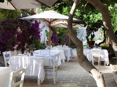 Outdoor-Café mit weißen gedeckten Tischen, Stühlen, Sonnenschirmen und blühenden Pflanzen im Hintergrund.