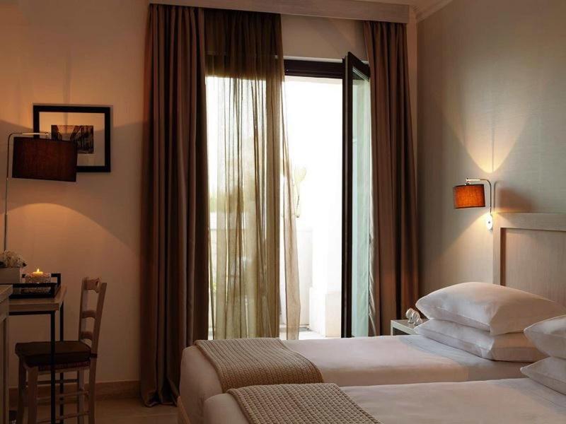 Gemütliches Schlafzimmer mit offener Balkontür, Doppelbett, Stuhl, Schreibtisch und warmem Licht.