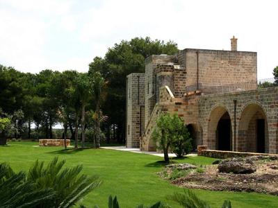 Ein Steingebäude mit Bögen steht neben einem gepflegten grünen Rasen und Palmen.