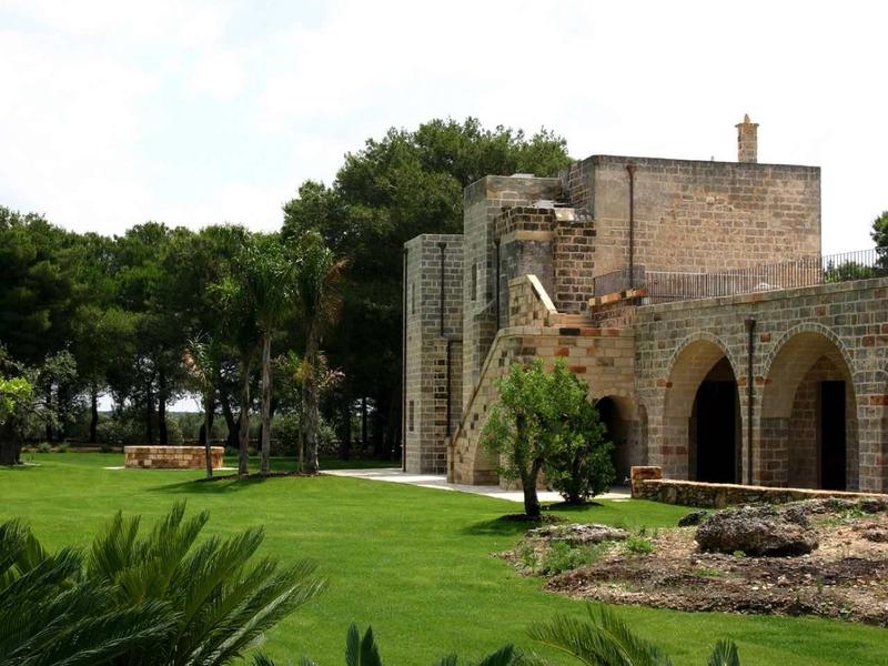 Ein Steingebäude mit Bögen steht neben einem gepflegten grünen Rasen und Palmen.