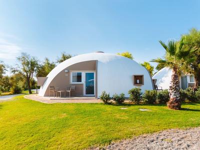 Weißes, kuppelförmiges Haus mit Terrasse, umgeben von grünem Rasen und Palmen.