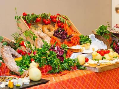 Bunt gedeckter Tisch mit frischem Gemüse, Kräutern, Brot und Käse auf rotem Tuch.