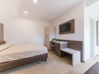 Modernes, schlichtes Schlafzimmer mit großem Bett, wandmontiertem Fernseher und hellem Boden.