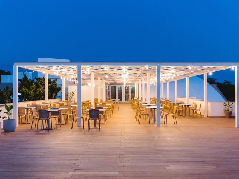 Offener, moderner Außenbereich mit Holzterrasse, weißen Möbeln und warmem Licht bei Dämmerung.