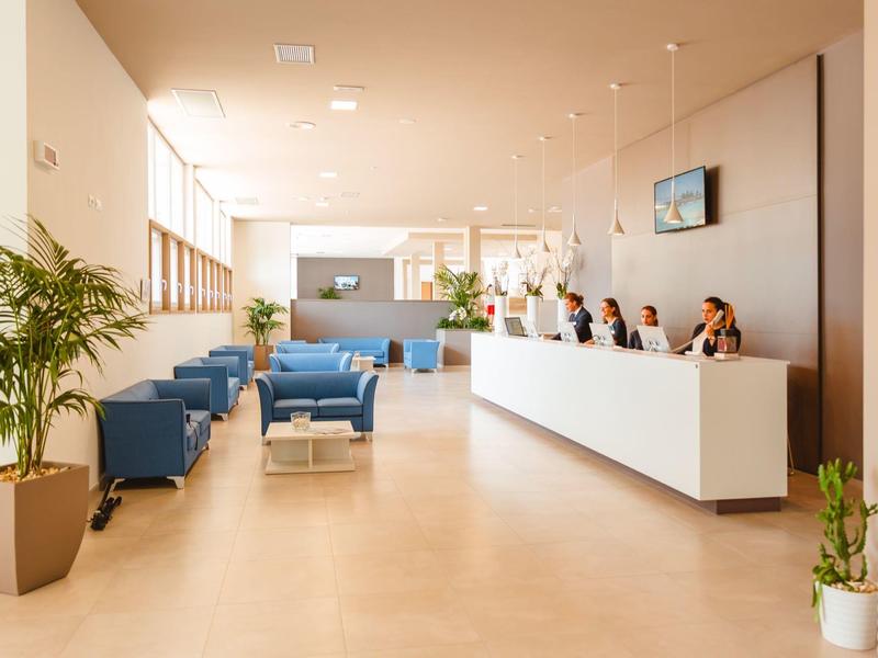 Großer heller Wartebereich mit blauen Sesseln, Rezeption und Pflanzen in weißen Töpfen.