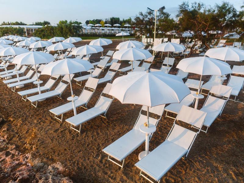 Reihe weißer Liegestühle mit weißen Sonnenschirmen auf felsigem Boden bei bewölktem Himmel.