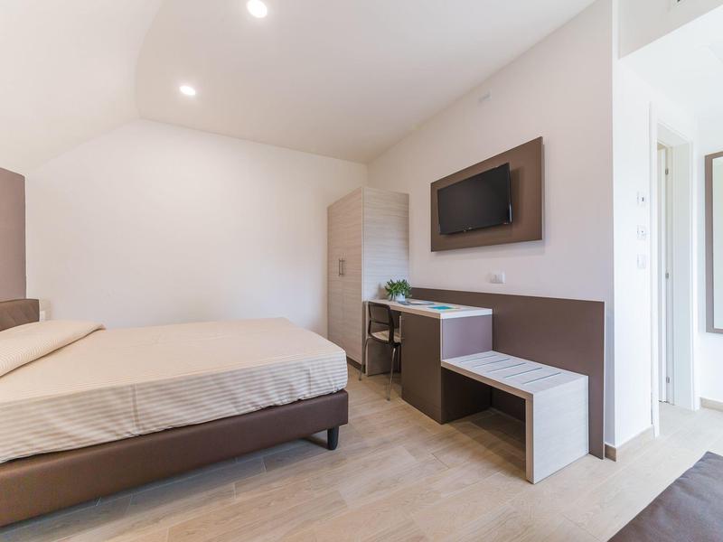 Modernes, schlichtes Schlafzimmer mit großem Bett, wandmontiertem Fernseher und hellem Boden.