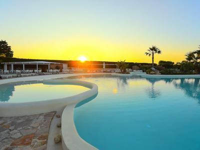 Großer Pool bei Sonnenuntergang mit Palmen, glattem Wasser und einem kleinen Becken im Vordergrund.