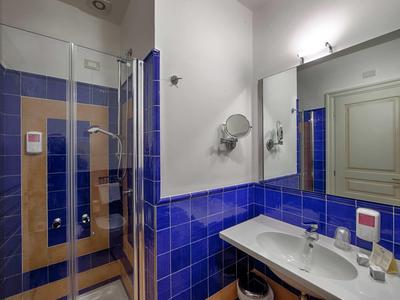 Badezimmer mit blauen Fliesen, großer Spiegel, Waschbecken und Glastür zur Dusche.