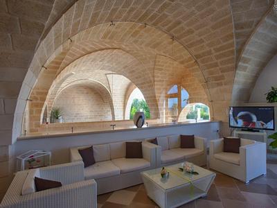 Großer Innenraum mit hellen Steinbögen, weißen Sofas, Kissen und dekorativen Pflanzen.