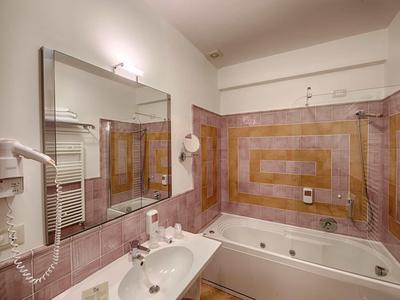 Modernes Badezimmer mit großer Badewanne, Spiegel, Waschbecken und braun-rot gemusterten Fliesen.