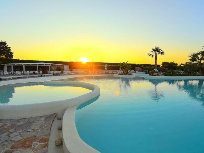 Großer Pool bei Sonnenuntergang mit Palmen, glattem Wasser und einem kleinen Becken im Vordergrund.