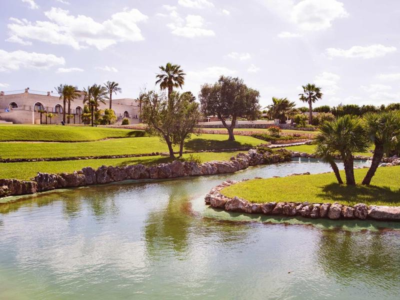 Grüner Park mit klarem Fluss, Palmen und bewölktem Himmel im Hintergrund.