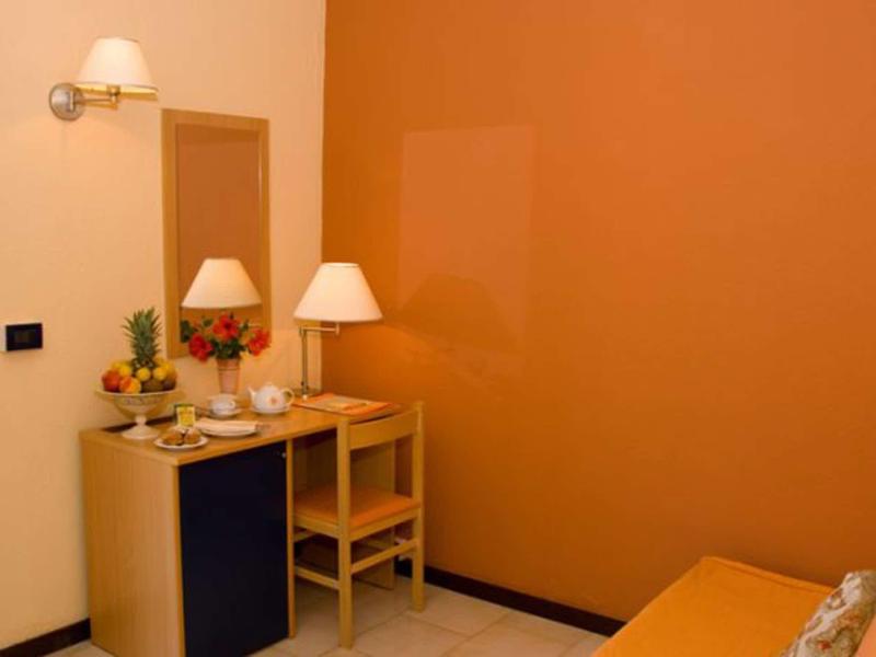 Kleines Zimmer mit orangener Wand, Schreibtisch, Stuhl, Lampen und Pflanzen auf dem Tisch.