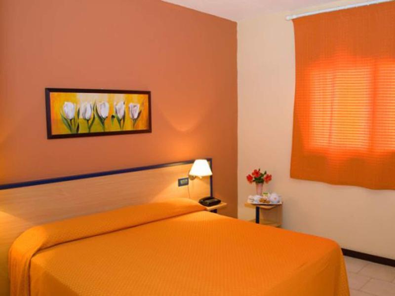 Schlafzimmer mit orangefarbenem Bett, Wand, Vorhang und weißem Nachttisch mit Blumen.