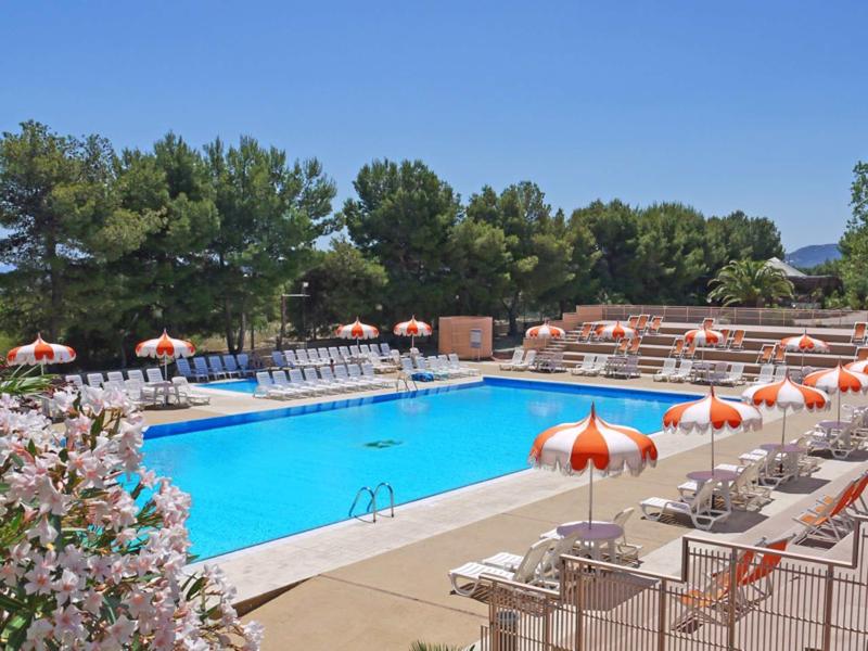 Großer rechteckiger Pool mit orangen Sonnenschirmen und Liegen, umgeben von grünen Bäumen.