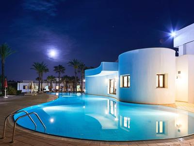 Runder Pool mit blauem Licht vor weißem Gebäude und Palmen bei Nacht unter hellem Mondschein.