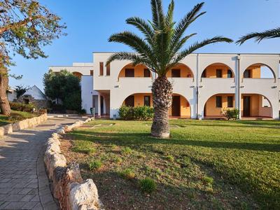 Hotelgebäude mit Bögen, Palme und gepflegtem Rasen unter klarem Himmel