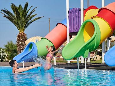 Kinder rutschen bunte Wasserrutschen in einen Pool mit blauer Wasseroberfläche bei Sonnenschein.