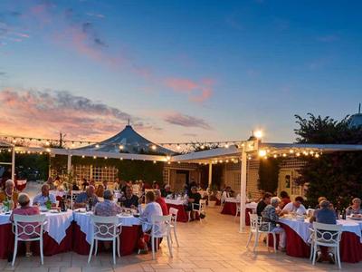 Draußen festlich gedeckte Tische mit weißen Hussen, Lichterketten und Menschen bei Sonnenuntergang.