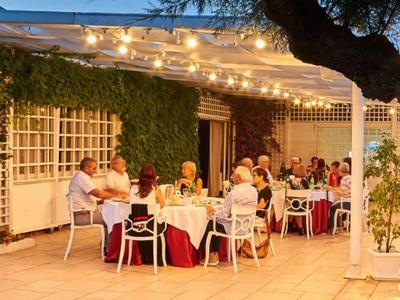 Menschen sitzen abends an dekorierten Tischen unter Lichterketten in einem Gartenrestaurant.