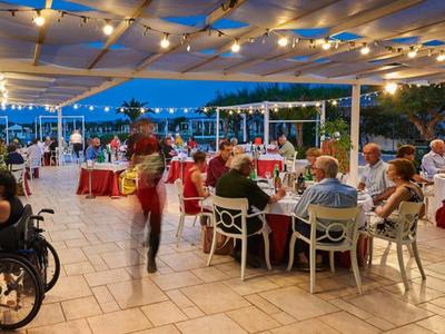 Restaurantterrasse mit Lichterketten, gedeckten Tischen und Gästen bei Abenddämmerung.