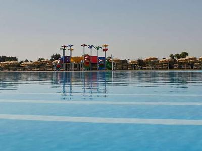 Großer Außenpool vor einem Wasserpark mit Rutschen unter blauem Himmel.