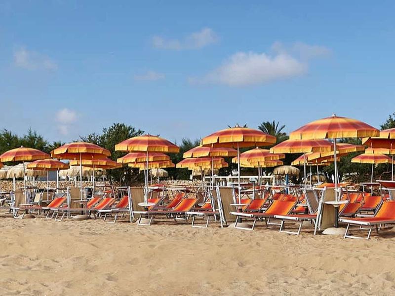Strand mit Sand, Reihen von Liegestühlen und orangenen Sonnenschirmen unter blauem Himmel.