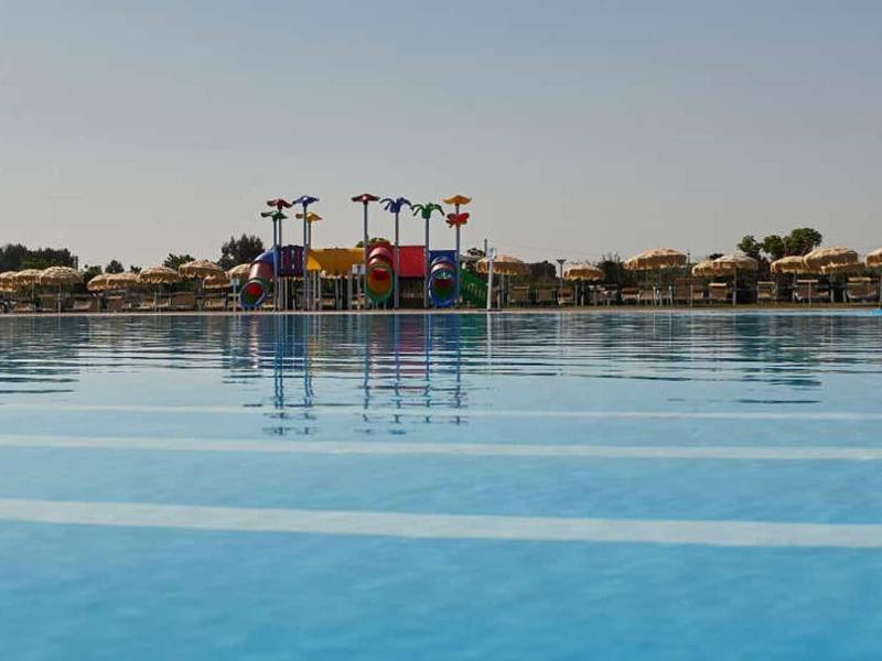 Großer, ruhiger Swimmingpool mit klarem, blauem Wasser und Wasserrutschen im Hintergrund bei Sonnenlicht.