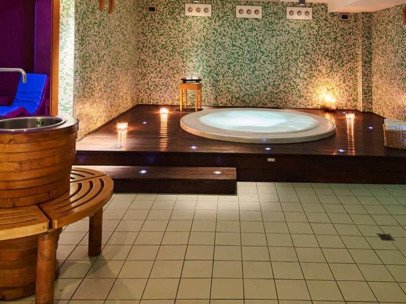 Eleganter Wellnessraum mit Mosaikfliesen, Rundwanne, Holzbottichen und warmem Licht.