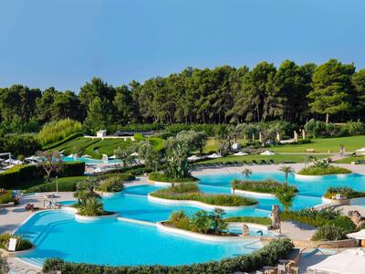 Duży obszar basenowy z krzywymi kształtami, leżakami i bujną zielenią w hotelowym kurorcie.