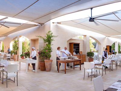 Hell beleuchtetes Restaurant mit weißen Tischen und Stühlen unter einer überdachten Terrasse.