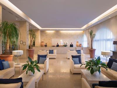 Elegante Hotellobby mit weißen Sofas, blauen Kissen und grünen Pflanzen in großen Töpfen.