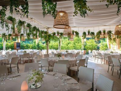 Großer, eleganter Veranstaltungsraum mit runden Tischen und hängenden Pflanzen, ideal für Feiern.