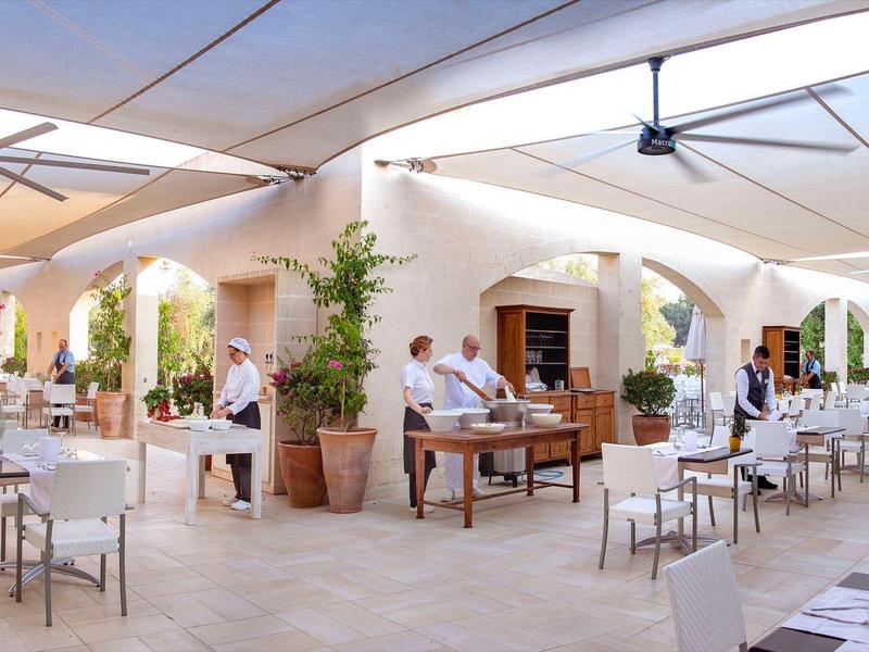 Hell beleuchtetes Restaurant mit weißen Tischen und Stühlen unter einer überdachten Terrasse.