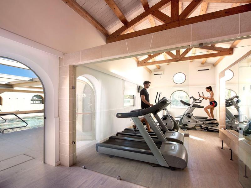 Moderne Fitnessgeräte in einem hellen Fitnessraum mit Blick auf den Poolbereich.