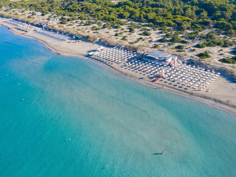 Luftaufnahme eines Strandes mit Sonnenschirmen und grüner Vegetation im Hintergrund.