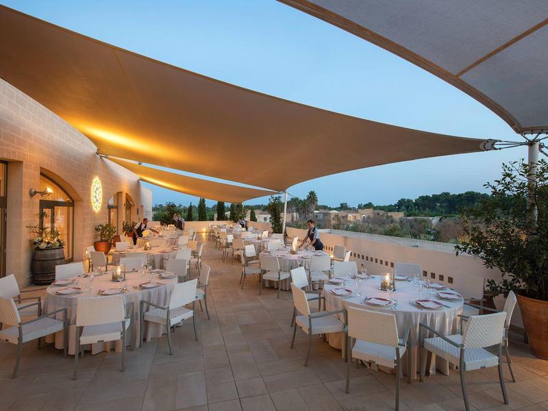 Elegante Außenterrasse eines Hotels mit gedeckten Tischen unter Sonnensegeln bei Abenddämmerung.