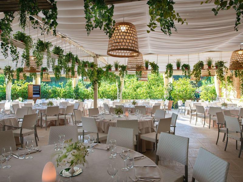 Großer, eleganter Veranstaltungsraum mit runden Tischen und hängenden Pflanzen, ideal für Feiern.