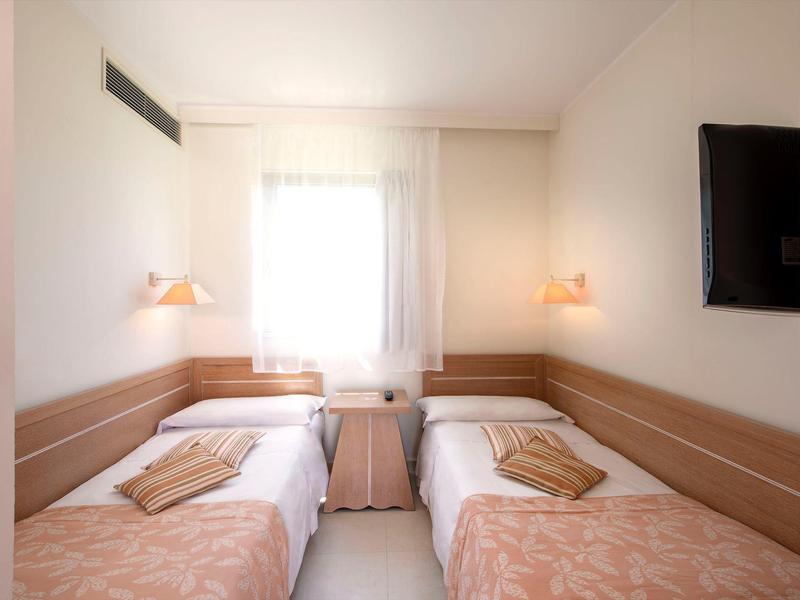 Kleines Hotelzimmer mit zwei Einzelbetten, Nachttisch und Wand-TV.