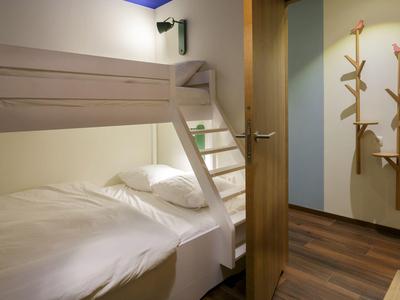 Gemütliches Zimmer mit Etagenbett und Holzboden, Holztür geöffnet zum Flur mit Hakenleisten.