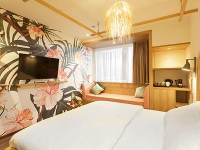 Helles Hotelzimmer mit Doppelbett, Wand mit floralem Muster und gemütlicher Fensterbank.