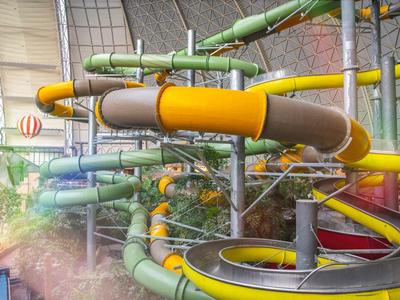 Innenansicht eines Wasserparks mit bunten, verschlungenen Wasserrutschen und einem gläsernen Dach.