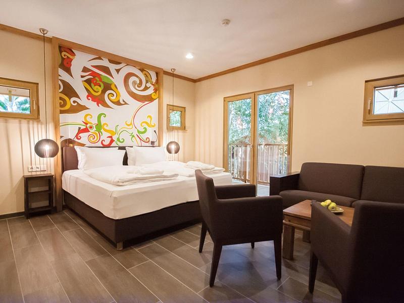 Gemütliches Hotelzimmer mit Bett, Sofa, Stühlen und einem großen dekorativen Wandbild.